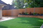 AFTER: A new curved planter wall was constructed and capped with single bullnose, new Marshall's Saxon paving installed and artificial lawn installed to finish.    