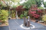 Small town house garden with a Japanese feel black limestone random paving installed with a centre slate water feature, Timber arbour constructed and garden planted with feature plants  