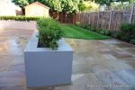 New lawn, planting, shed and fence patio was constructed using fossil sandstone in 4 sizes laid to a random pattern with a curved block planter wall painted in gun ship grey and planted with a topiary hedge.