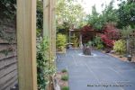 Small town house garden with a Japanese feel black limestone random paving installed with a centre slate water feature, Timber arbour constructed and garden planted with feature plants  