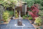 Small town house garden with a Japanese feel black limestone random paving installed with a centre slate water feature, Timber arbour constructed and garden planted with feature plants  